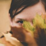 selective focus photo of woman hiding on green and brown leafed plant